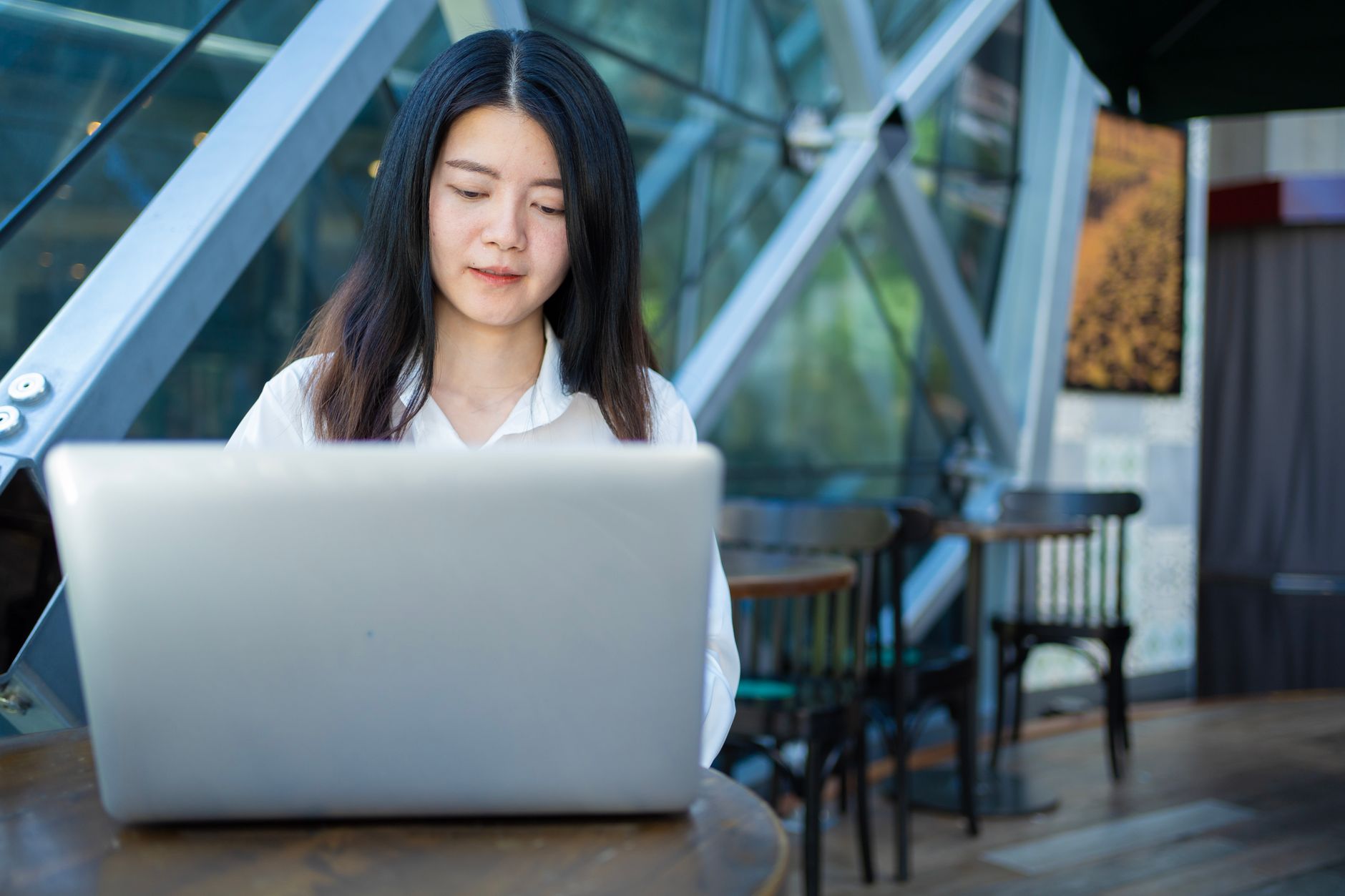 Asian woman working on a laptop in a modern cafe, exemplifying digital entrepreneurship and remote work.