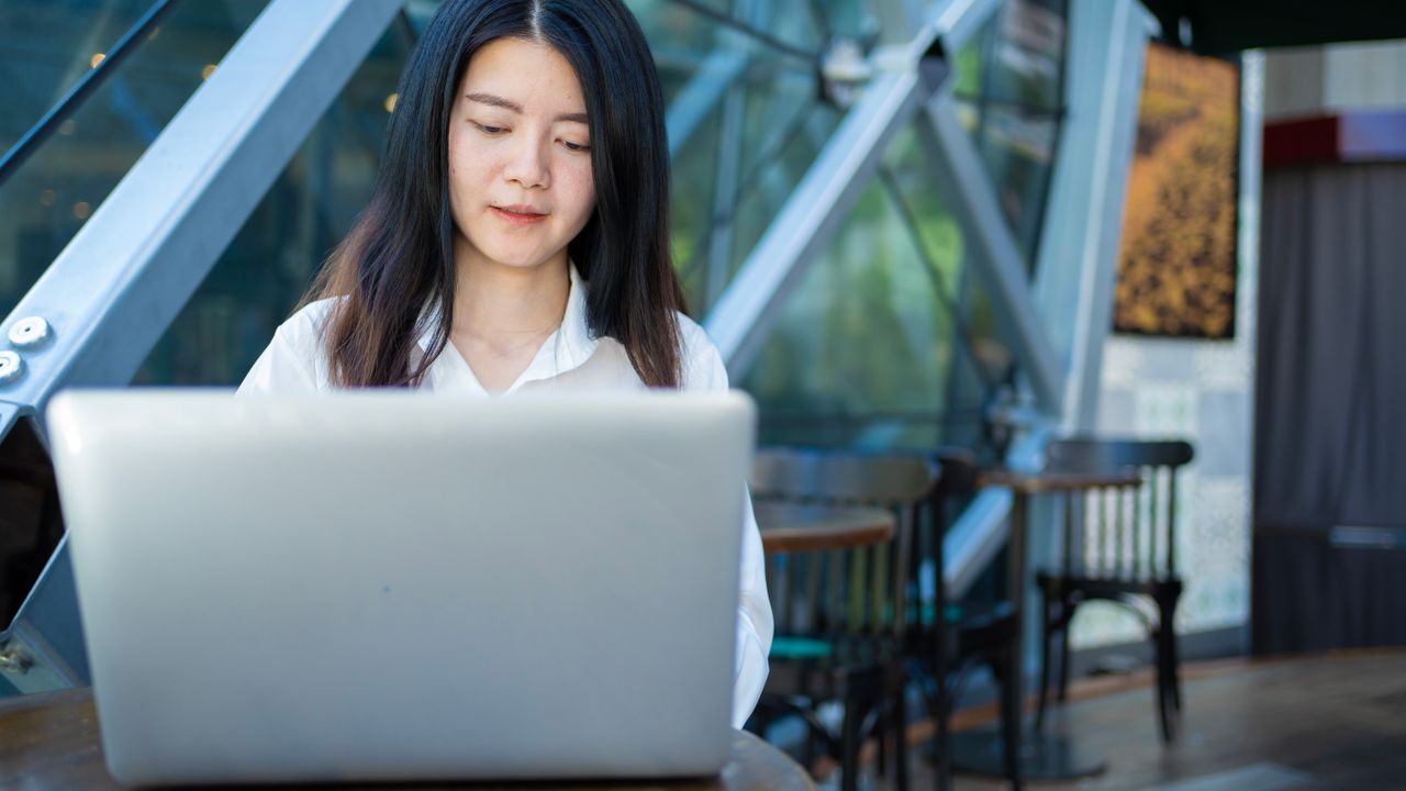 An Asian freelancer working on a laptop in a bright cafe.