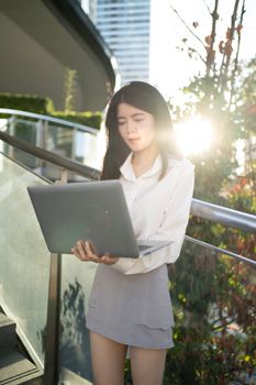 Asian woman working on a laptop outdoors in Bangkok, Thailand, showcasing modern lifestyle.