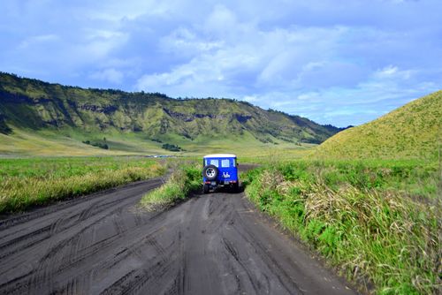Free Blue SUV traverses the rugged terrain of Mount Bromo, showcasing natural beauty and adventure. Stock Photo