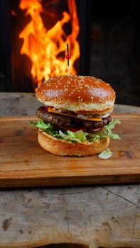 Delicious sesame seed bun cheeseburger with lettuce and sauce, set on a wooden board with a fiery backdrop.