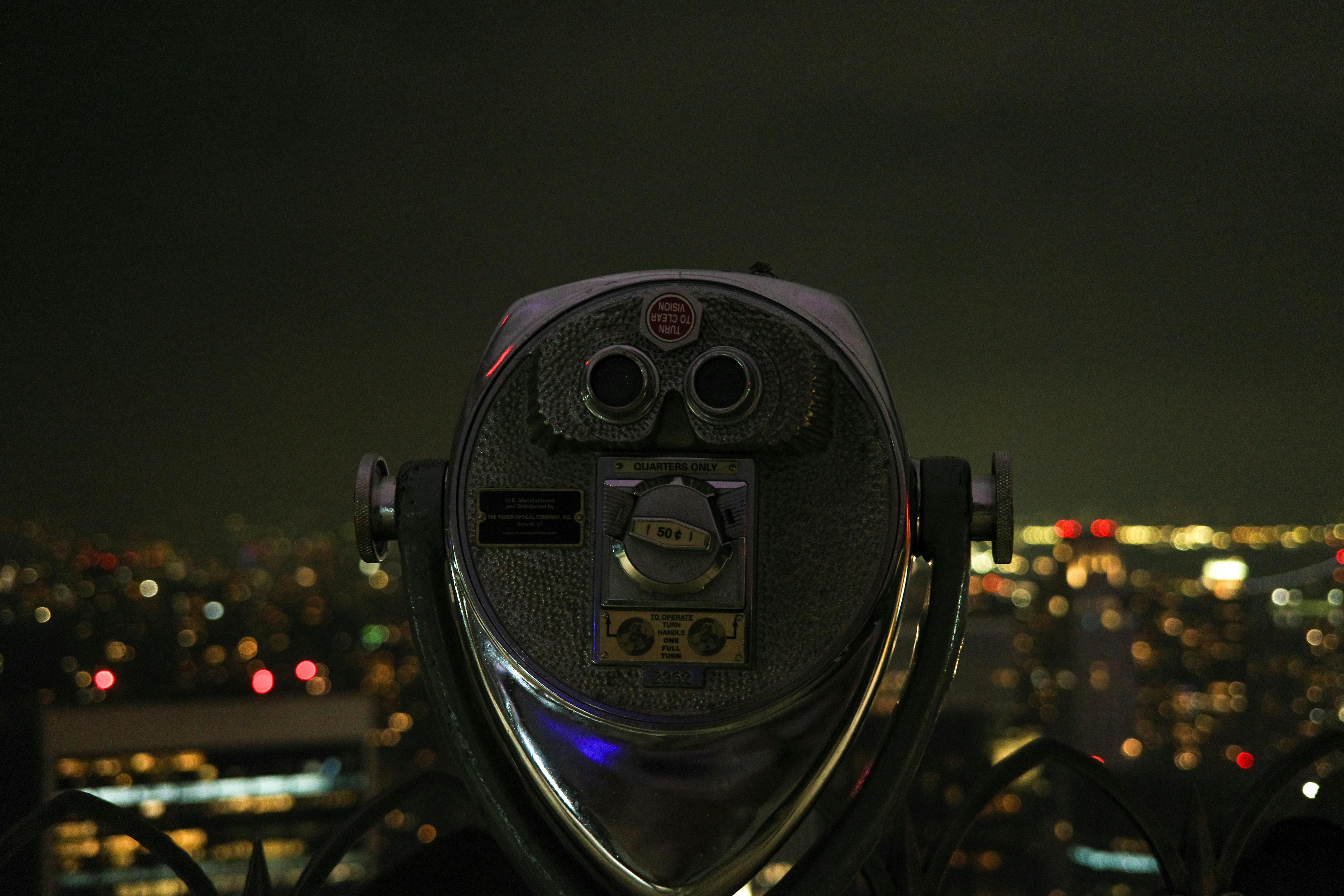 Kostnadsfria Utsikt genom myntdriven kikare över en stadssilhuett på natten med bokeh-ljus. Stock foto