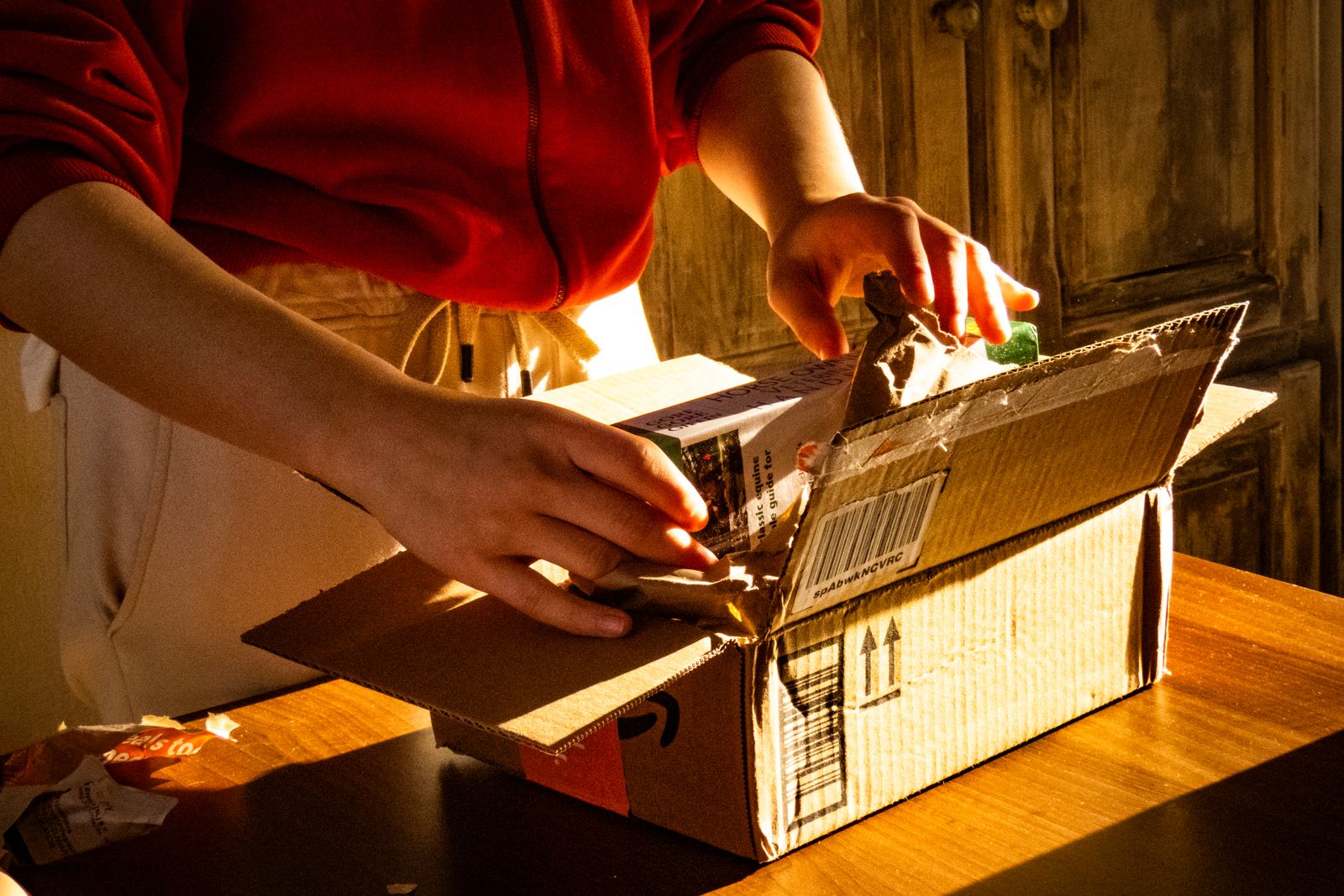 A pair of hands carefully unboxing a parcel in warm indoor lighting, capturing anticipation.