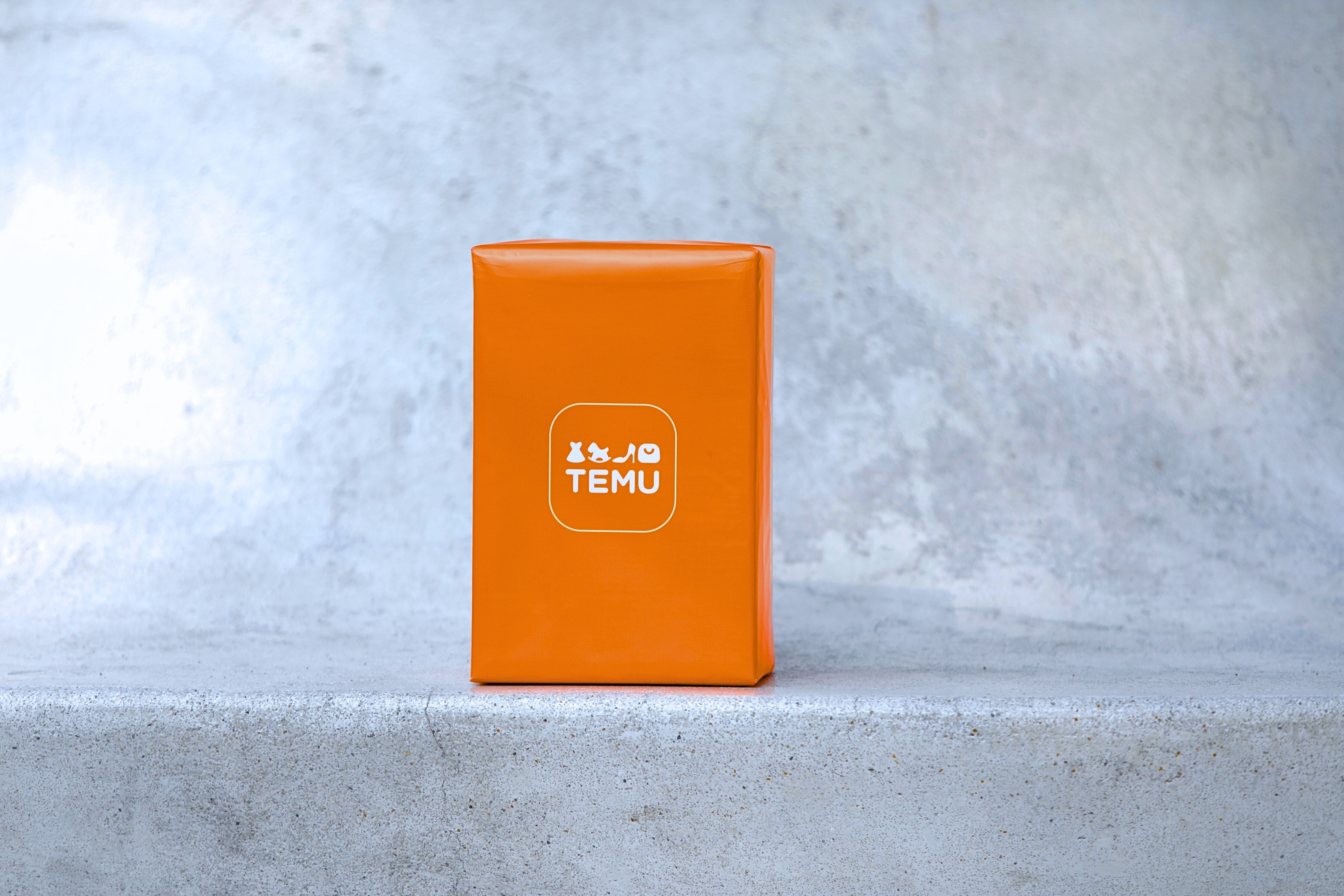 Bright orange parcel with Temu logo on a concrete surface, suitable for ecommerce themes.