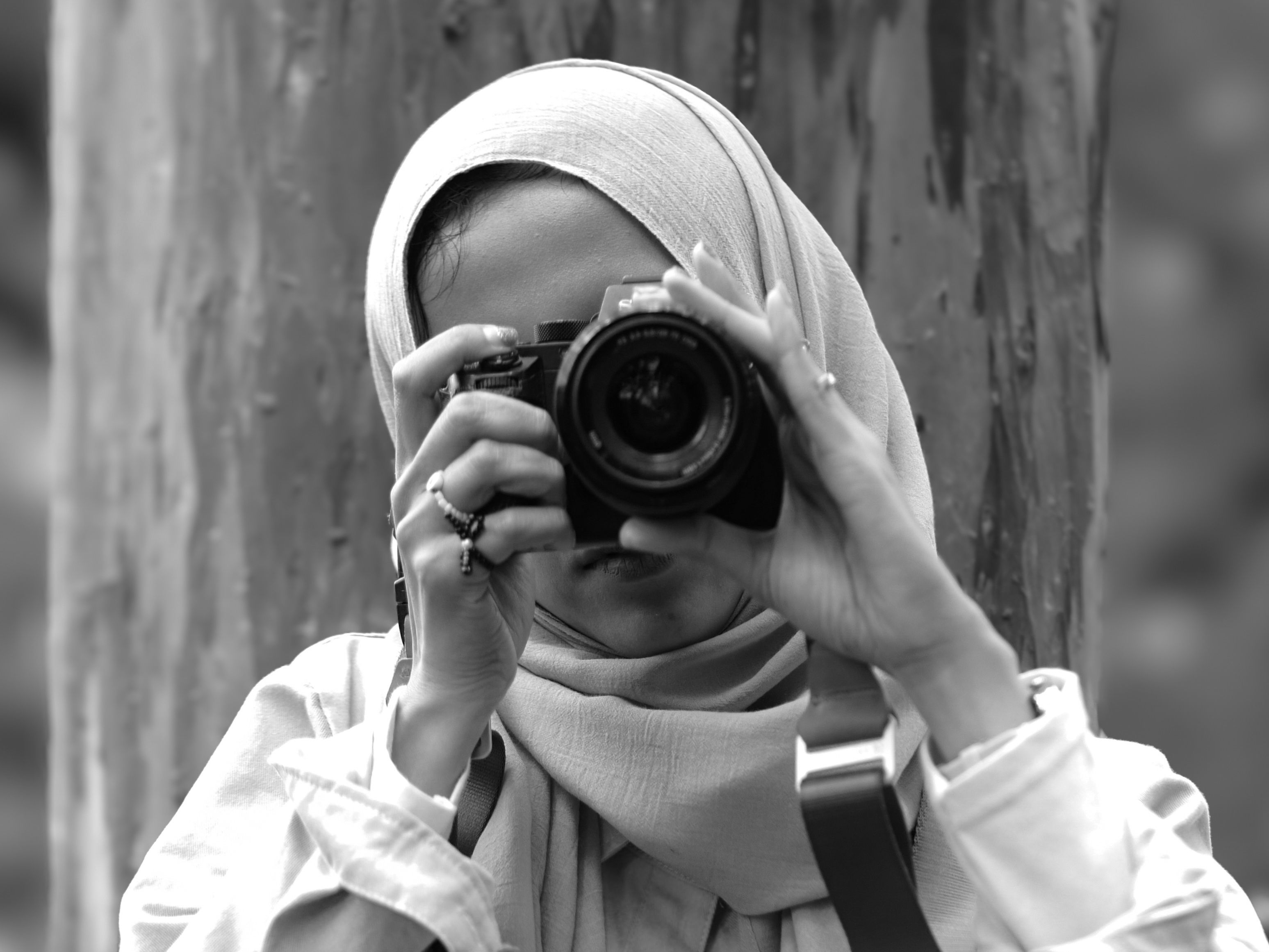 Black and white photo of a woman photographer taking a picture outdoors.