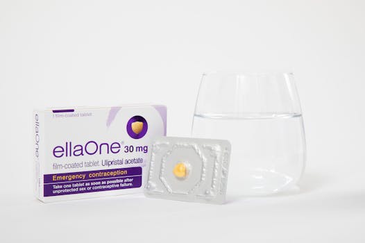 An image of the EllaOne emergency contraceptive pill with a glass of water indoors.