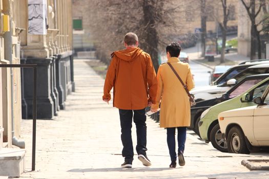 A couple holding hands walking on a sunlit street in Lviv, Ukraine, showcasing urban life.