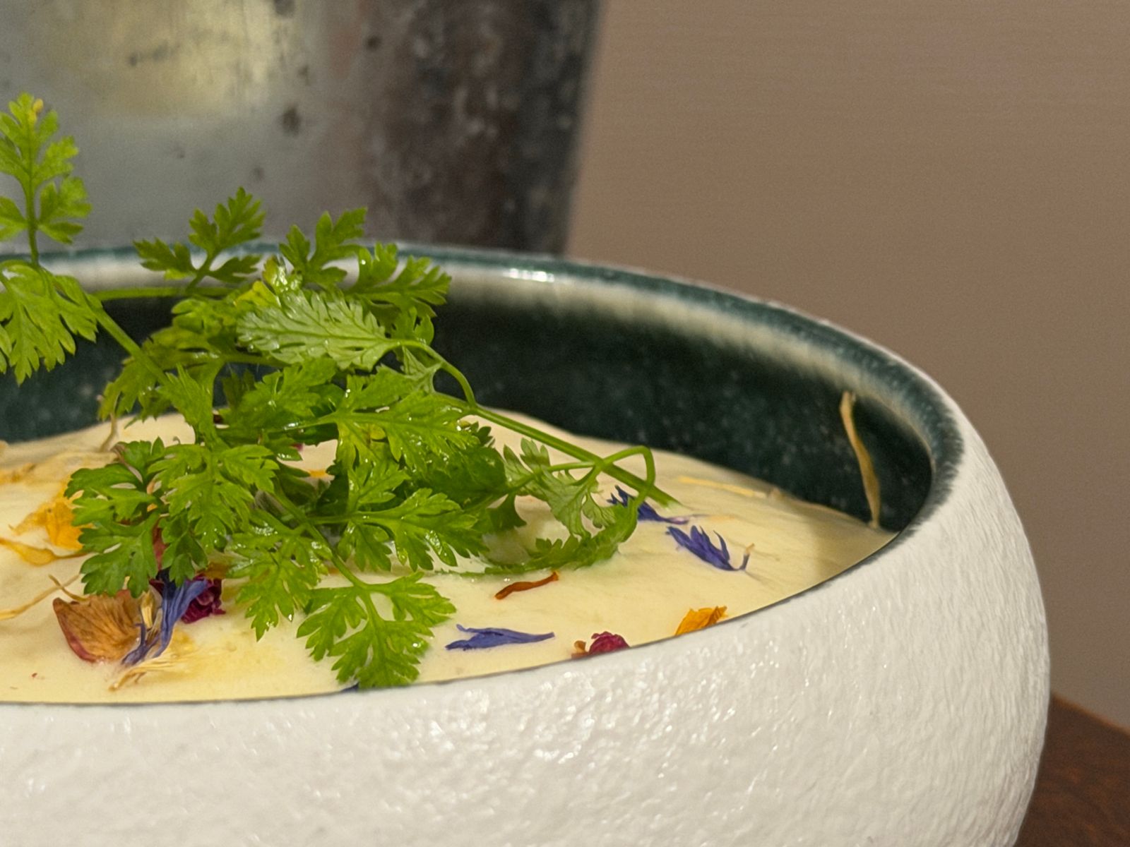 Velouté dans un bol blanc texturé garni de cerfeuil et de pétales