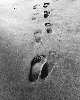 Black and white image of footprints marking a simple journey on a sandy beach.