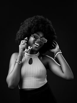 Elegant black and white portrait of a woman with afro hair and retro accessories, smiling joyfully.