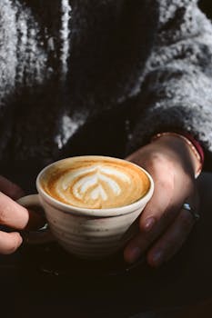 Close-up of hands holding a latte with heart-shaped art. Warm and inviting.
