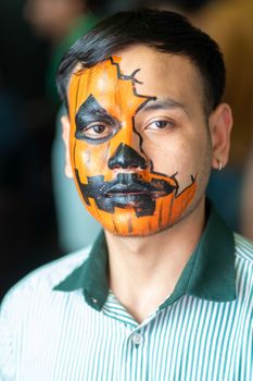 Close-up portrait of a man with pumpkin-themed Halloween face paint, striking design.