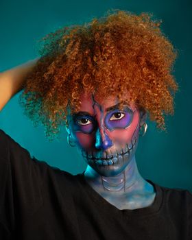 Model with colorful skeleton makeup poses against teal backdrop, showcasing artistic creativity.