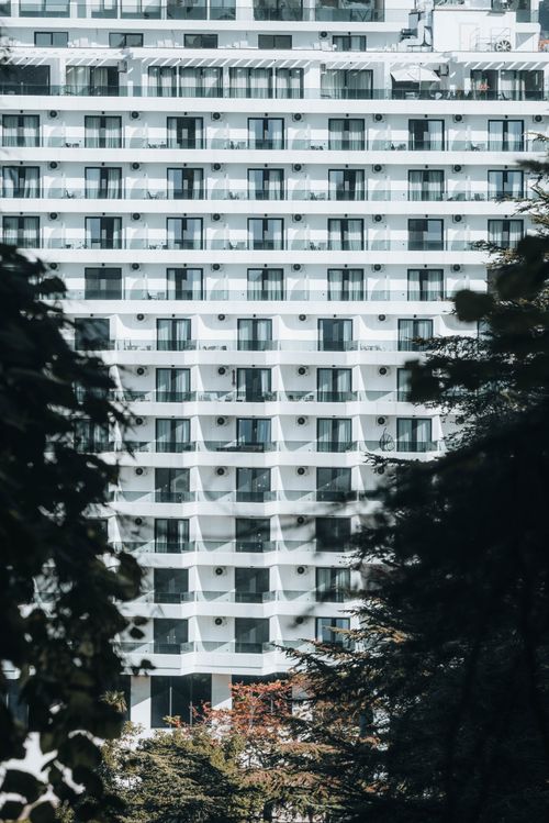 Free Contemporary high-rise building with glass balconies, framed by greenery. Stock Photo