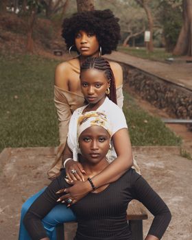 Stylish portrait of three black women posing elegantly outdoors in a serene park setting.