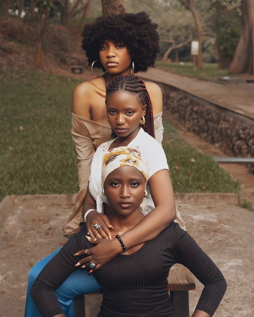 Stylish portrait of three black women posing elegantly outdoors in a serene park setting.