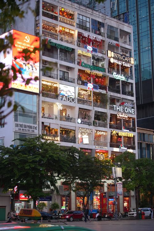 Free A bustling city scene with a multi-story building showcasing various cafes and shops in evening light. Stock Photo