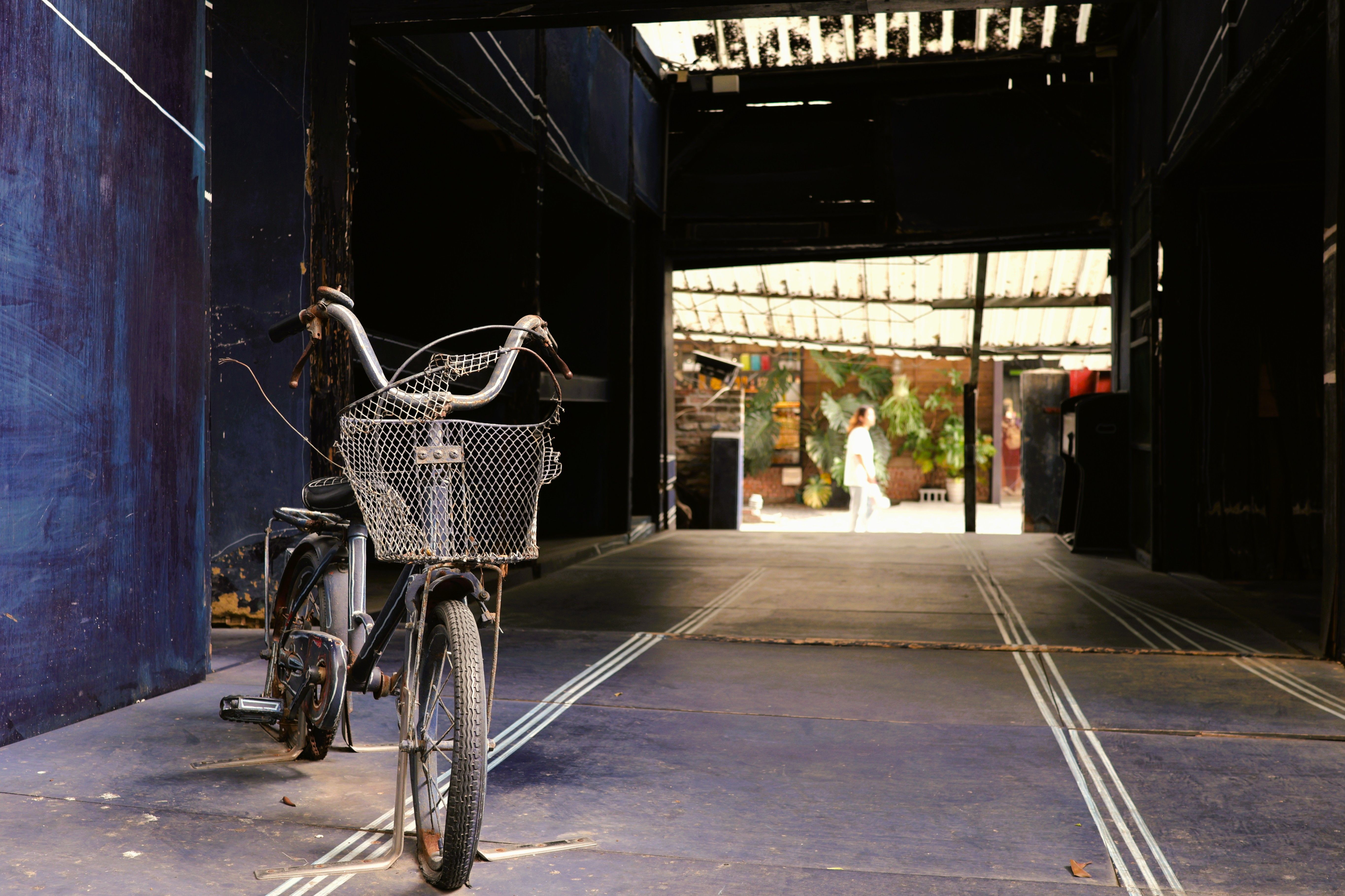 A vintage bicycle with a basket parked in a narrow alley in Taiwan, with a person walking in the background.