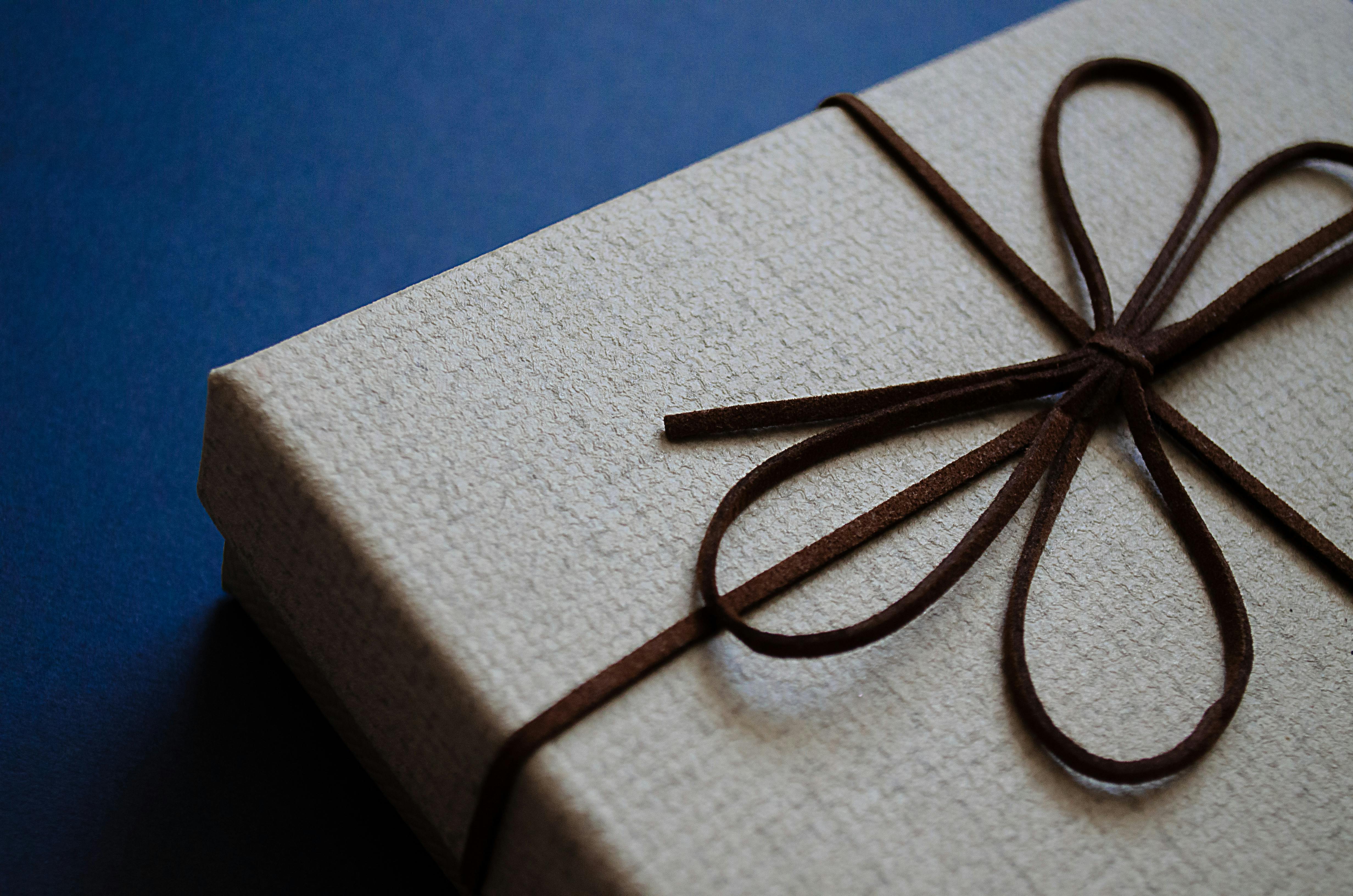 Close-up of an elegant gift box with a brown leather bow on a blue surface, perfect for special occasions.