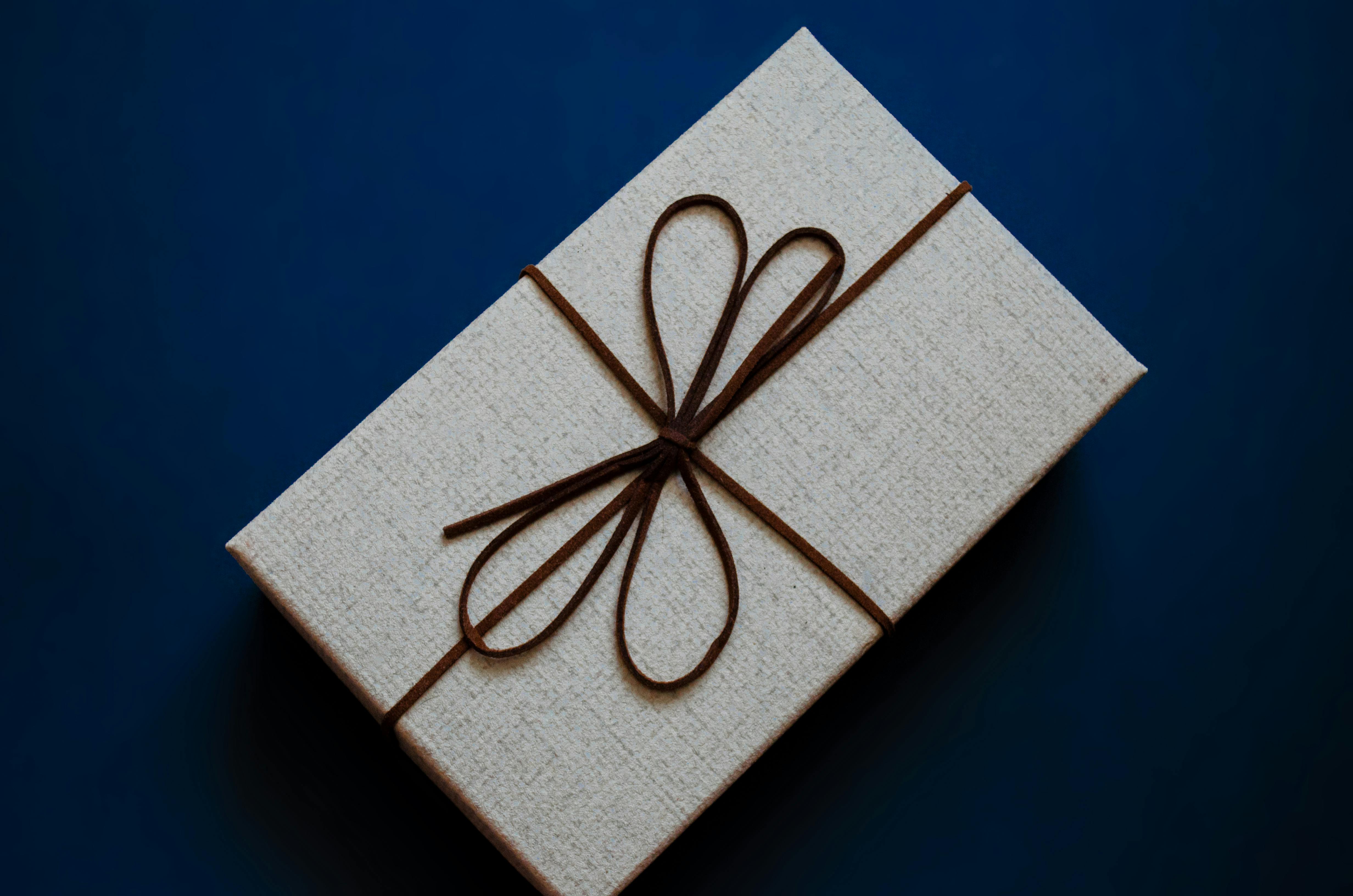 gratis Een stijlvolle geschenkdoos, verpakt met een bruin lint op een diepblauwe ondergrond, perfect voor feestelijke gelegenheden. Stockfoto