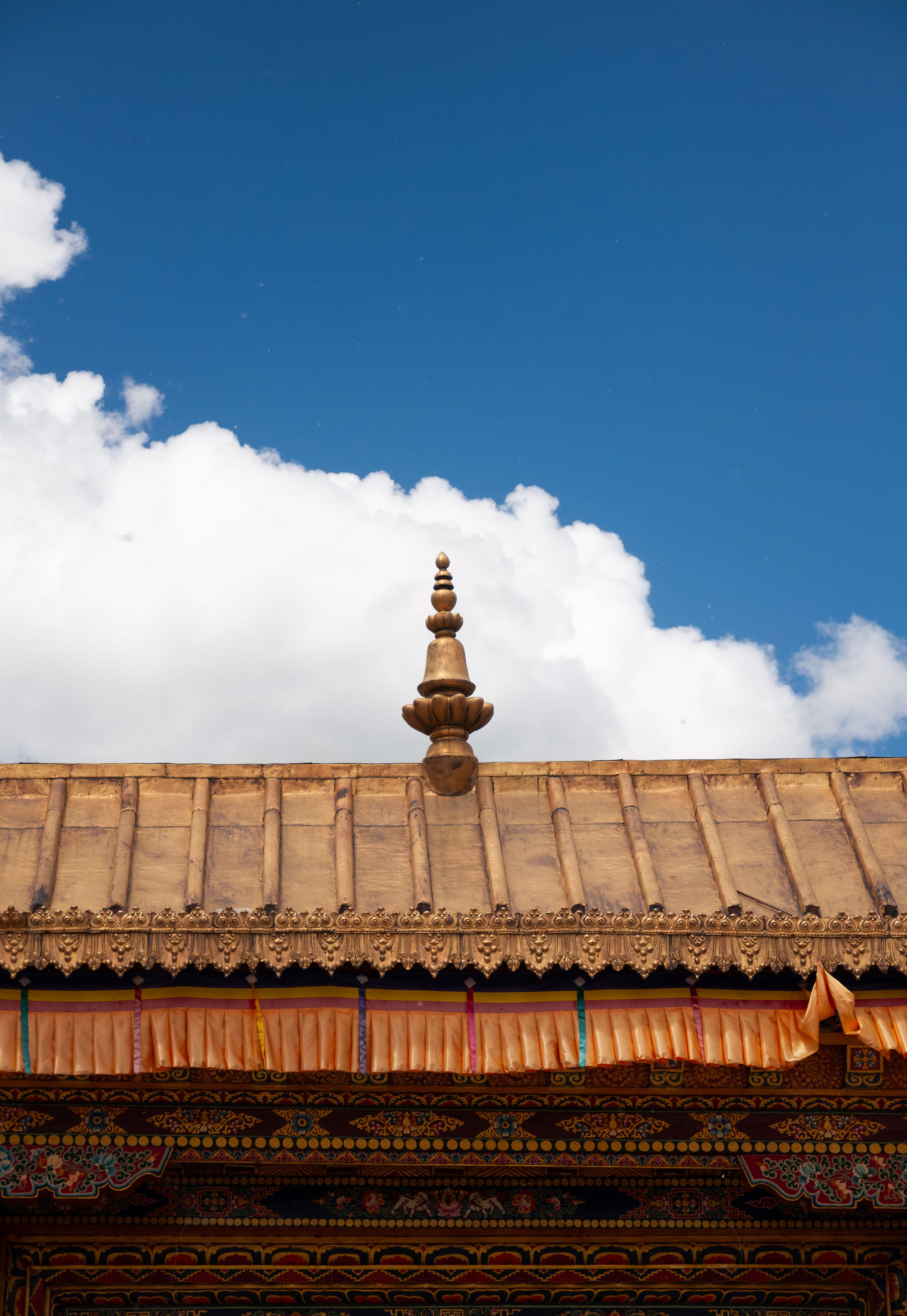 A close-up of a traditional Tibetan temple roof with intricate designs under a clear blue sky and white clouds.