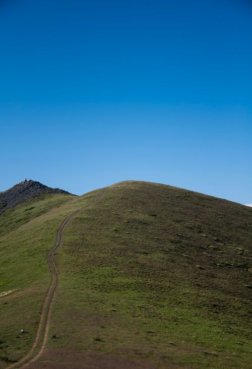 Free A serene green hill with a winding path against a bright blue sky, capturing nature's simplicity. Stock Photo
