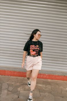 Stylish woman in casual summer outfit walking past a closed shop shutter.