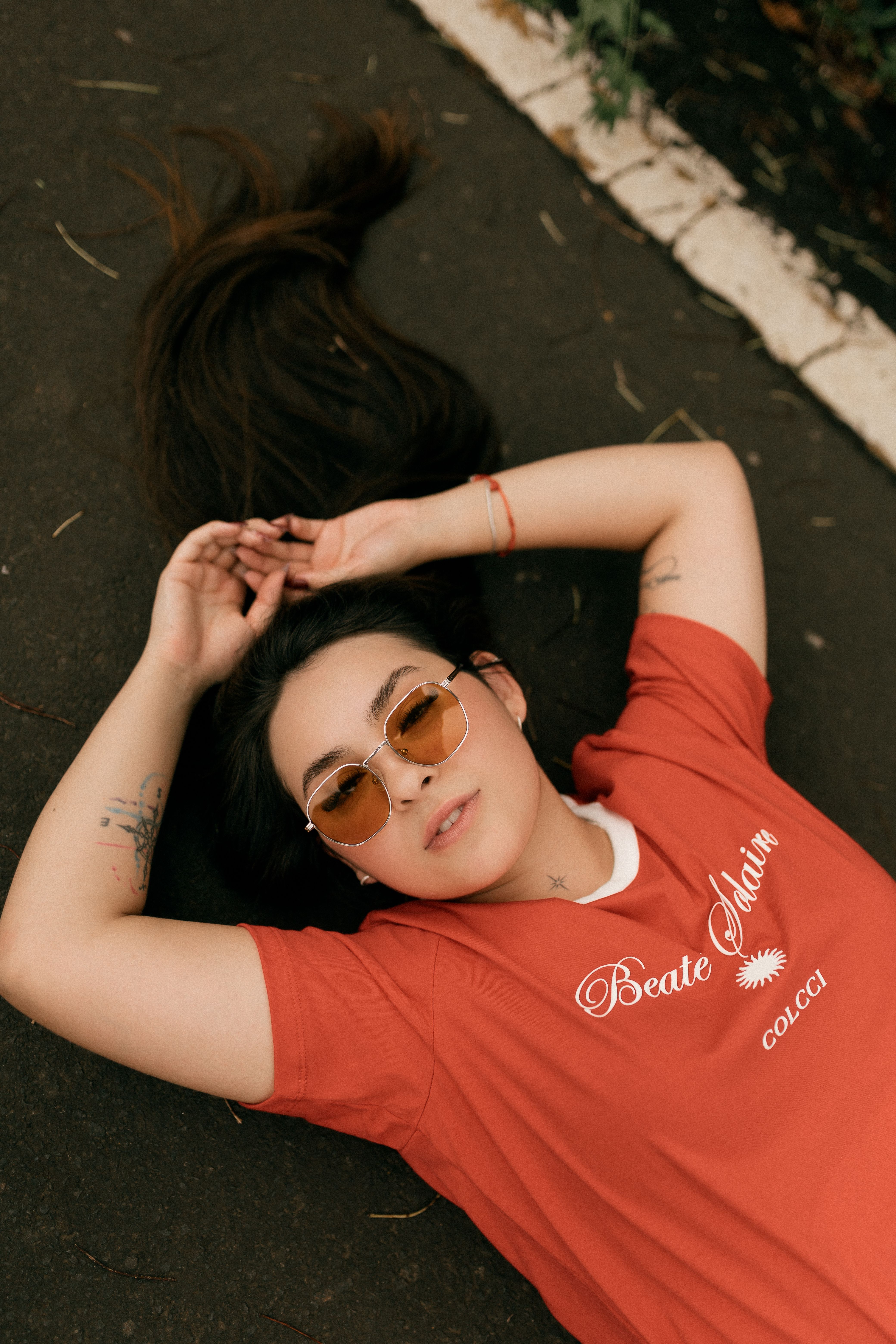 A young woman in sunglasses and a red shirt lies relaxed on a paved path.
