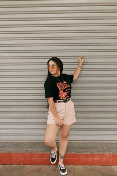 Fashionable young woman in casual outfit posing against a metal shutter.