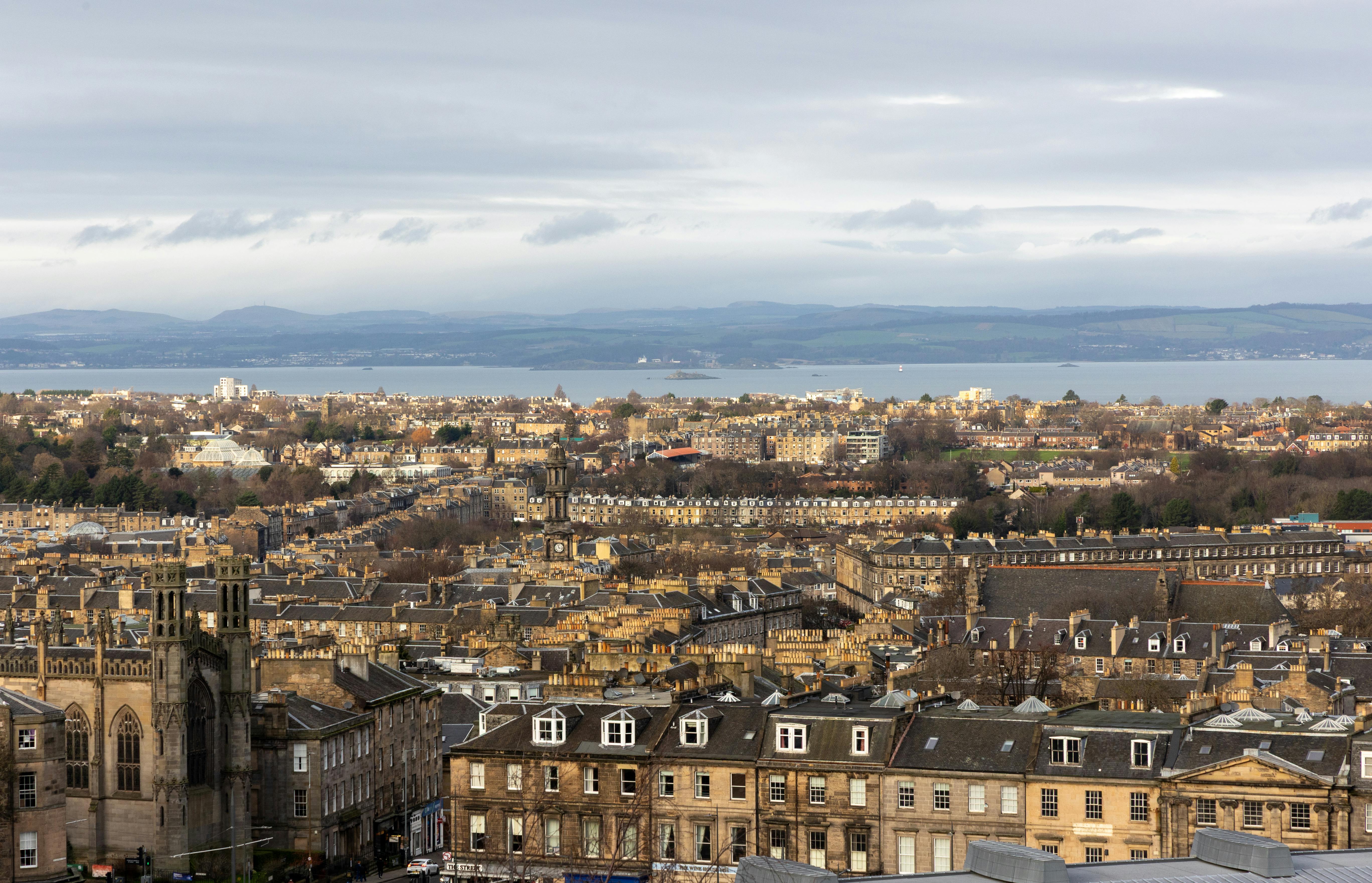 A scenic winter view of Edinburgh, showcasing historic architecture and cityscape with distant hills.
