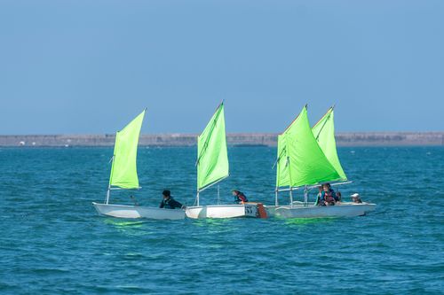Free Children sailing small boats with green sails on a sunny day at sea, fostering teamwork and skills. Stock Photo