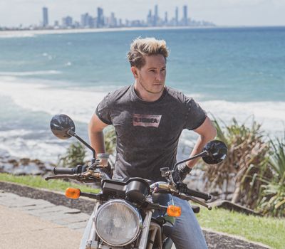 Stylish man on a vintage motorcycle with Gold Coast skyline in the background.