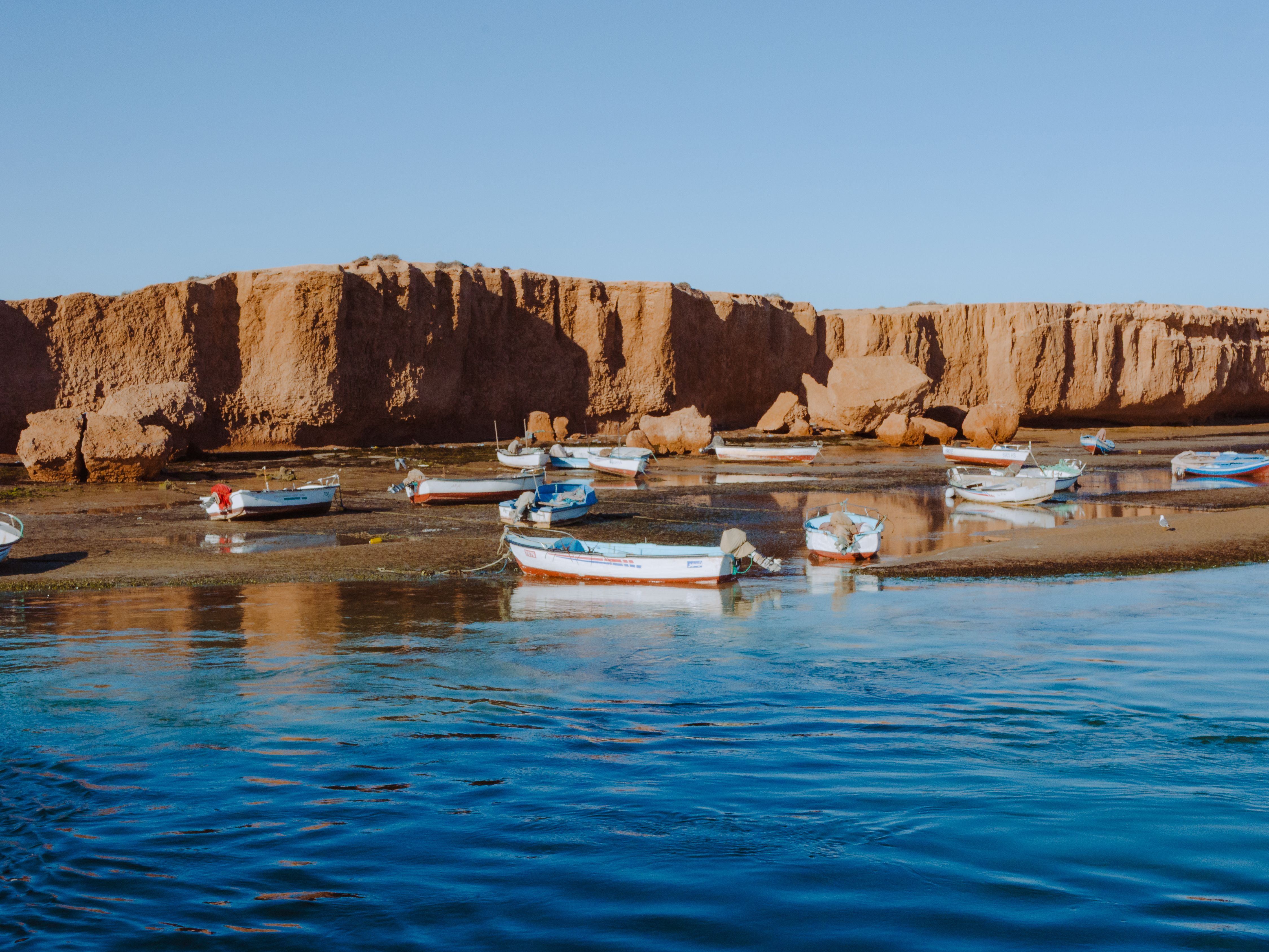 Fishing boats rest on calm waters against the rocky cliffs in Médenine Governorate, Tunisia.