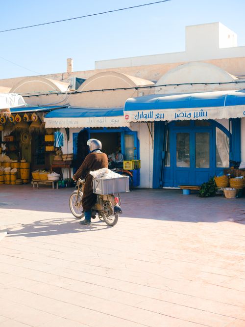 Free A man on a scooter passing shops in Médenine, Tunisia, showcasing local culture. Stock Photo