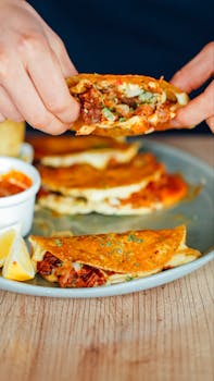 Close-up of a person enjoying a flavorful quesadilla with various fillings on a wooden table.