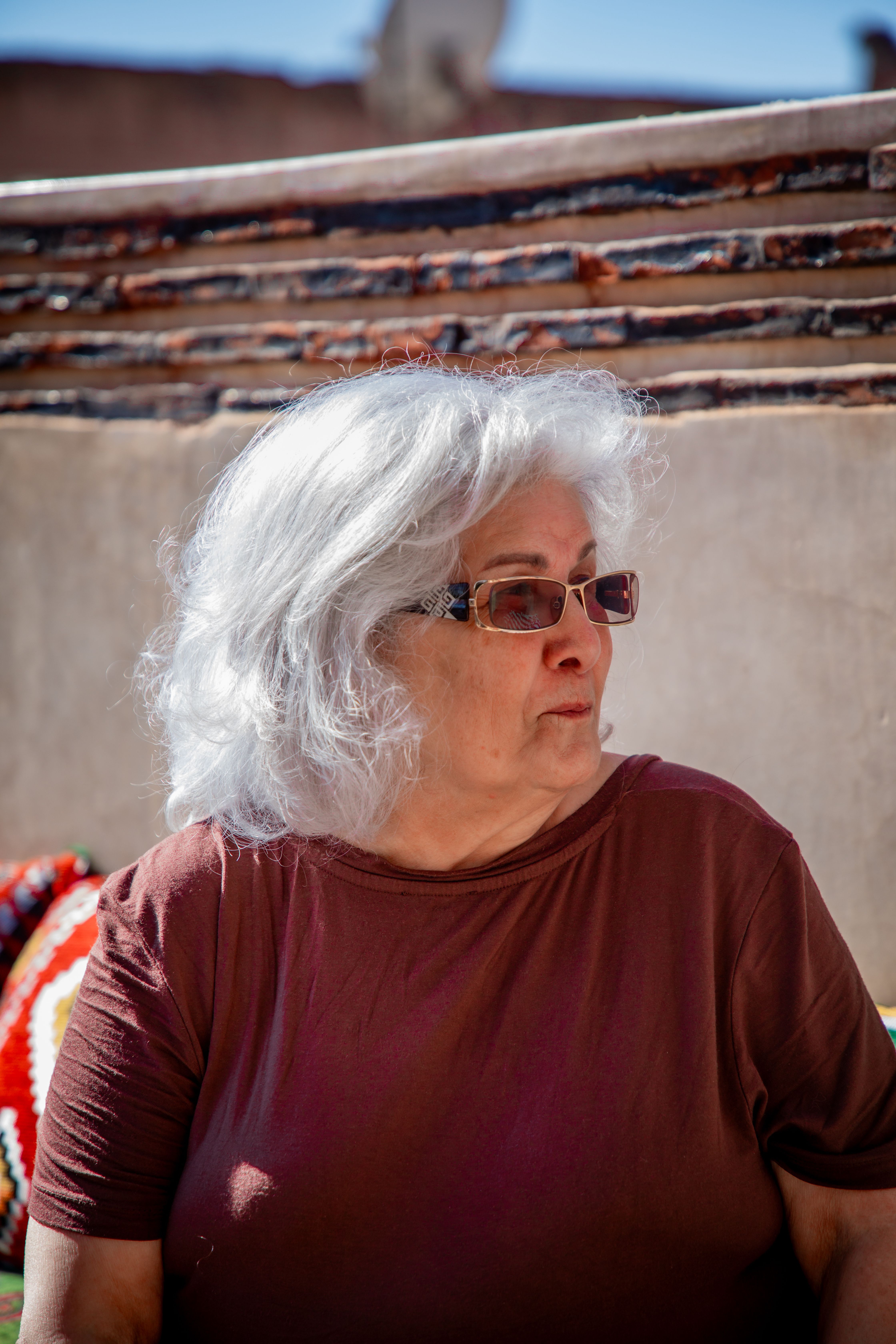 Elderly woman with sunglasses on a Marrakesh rooftop, showcasing local architecture.