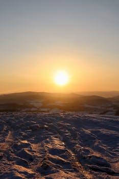 Serene winter sunset over a snowy landscape with hills in the distance.