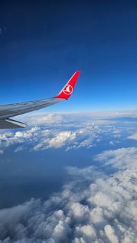 Aerial view of airplane wing above clouds with clear blue sky.