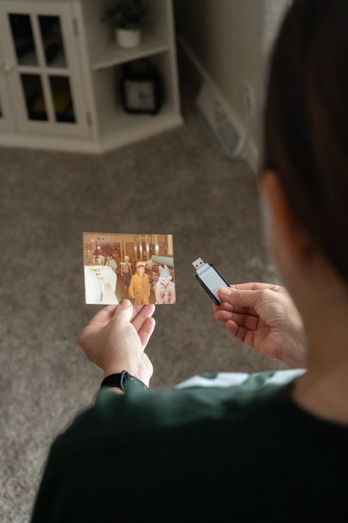 Free Person comparing a vintage photo with a USB drive, representing digital archiving. Stock Photo