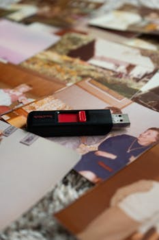 A black USB drive placed over assorted vintage family photos, evoking nostalgia.