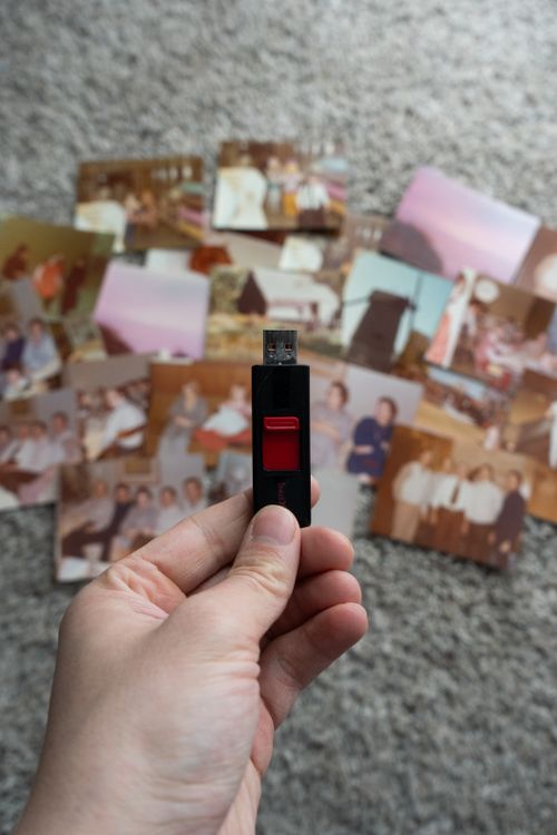 Free A USB drive held above a collection of vintage family photos on a carpet, illustrating digital photo storage. Stock Photo