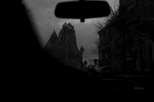 A moody black and white shot of mountains and architecture through a car window.
