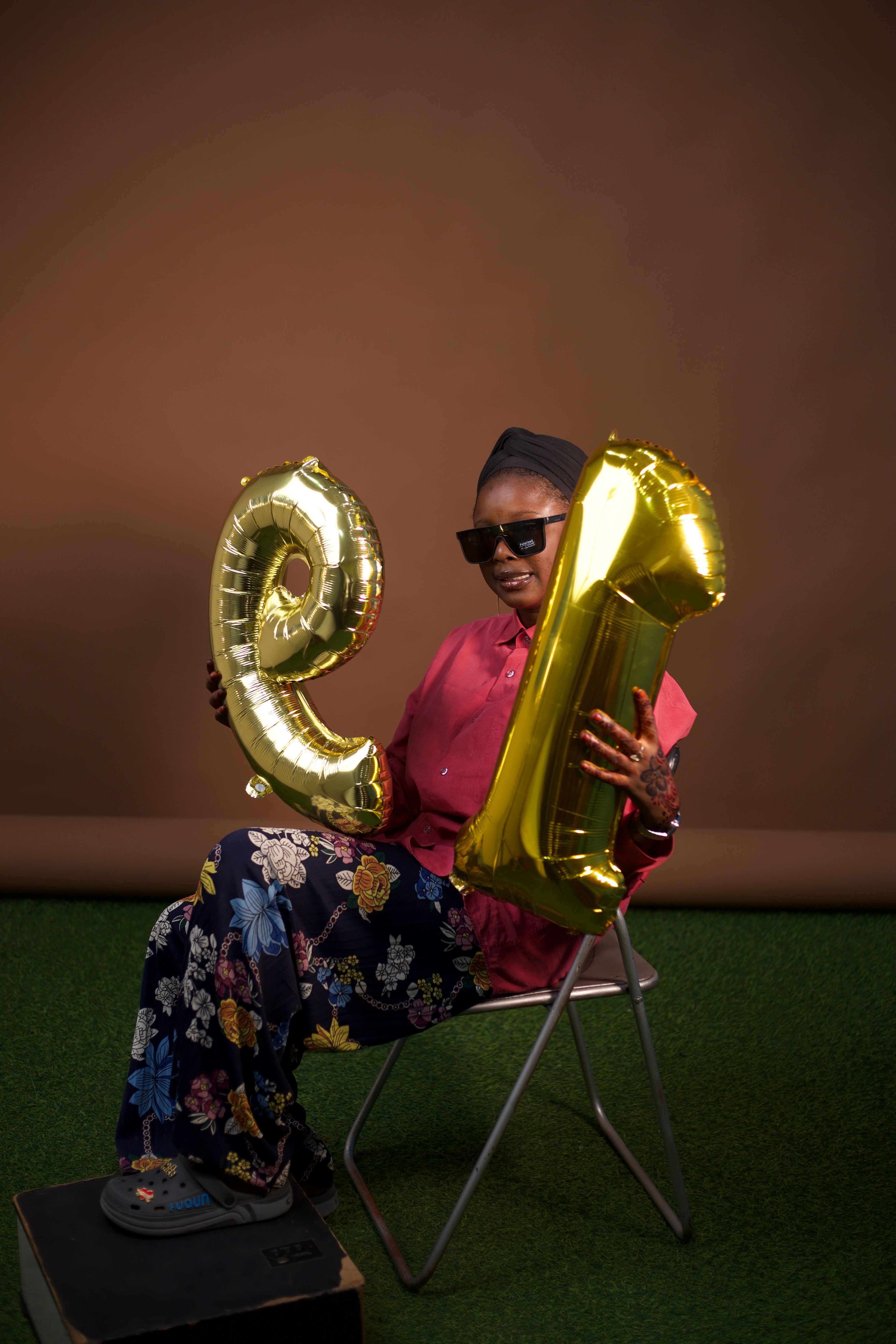 Smiling woman with gold balloons and sunglasses celebrates indoors.