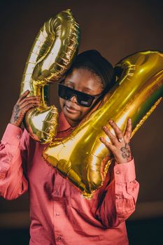 Person celebrating with golden number balloons and sunglasses.