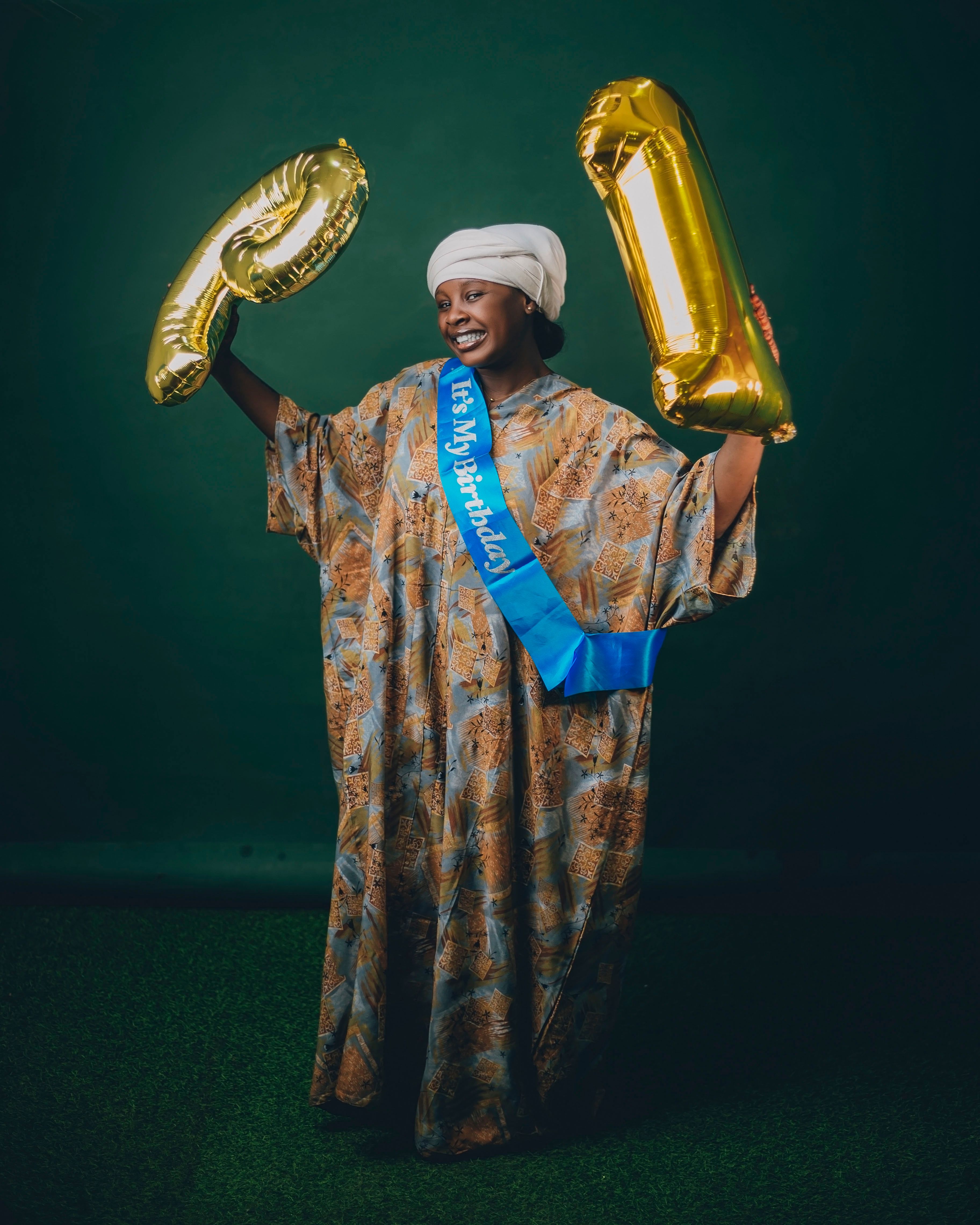 Joyful woman celebrating birthday with balloon numbers against green background.