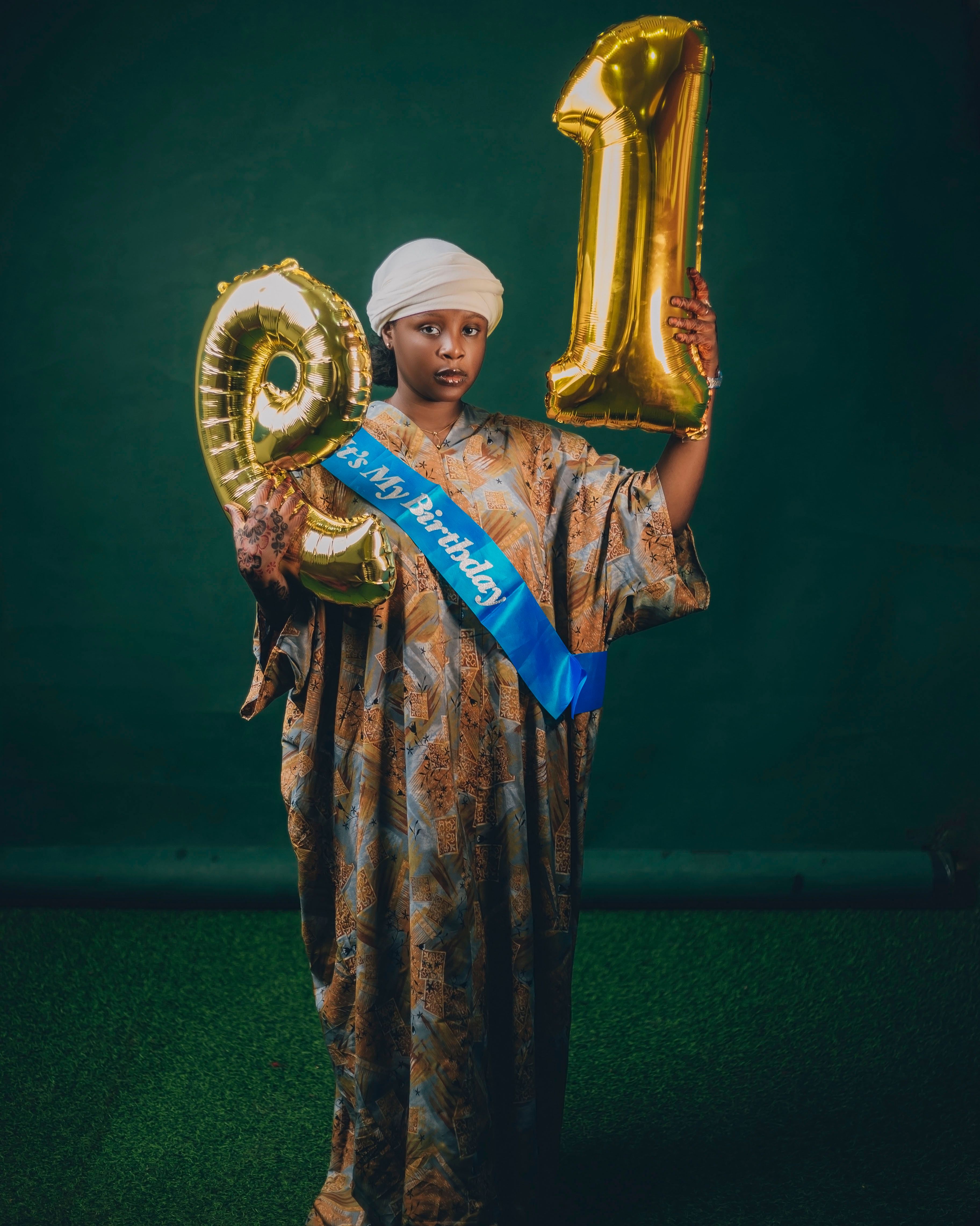 Woman celebrating 21st birthday with gold balloons and a sash.