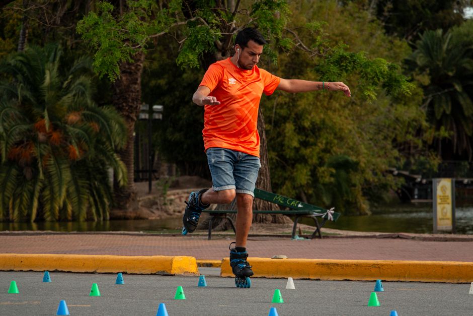 Man wearing an orange shirt roller skating through slalom cones outdoors, showcasing skill and balance.