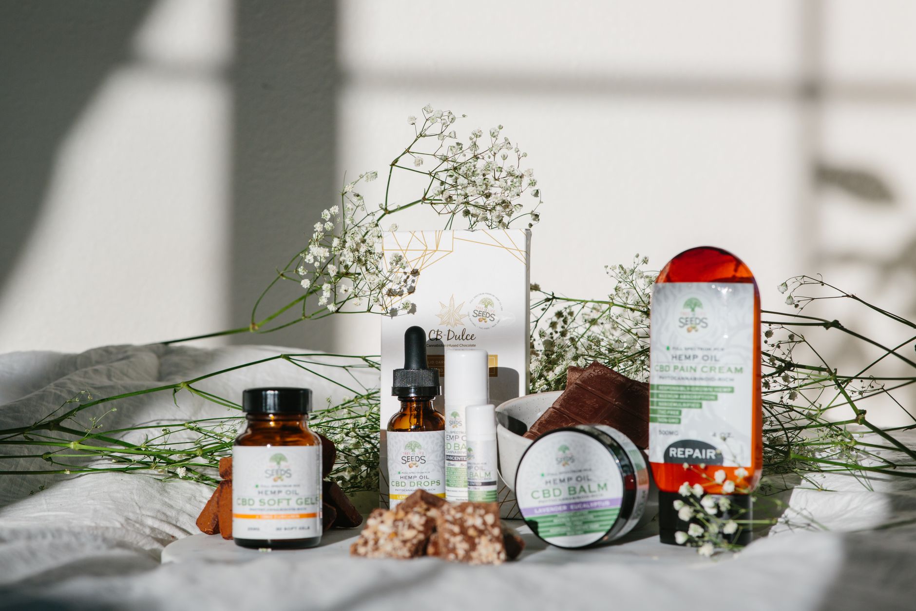 A collection of CBD and hemp products displayed with delicate floral accents in natural light.