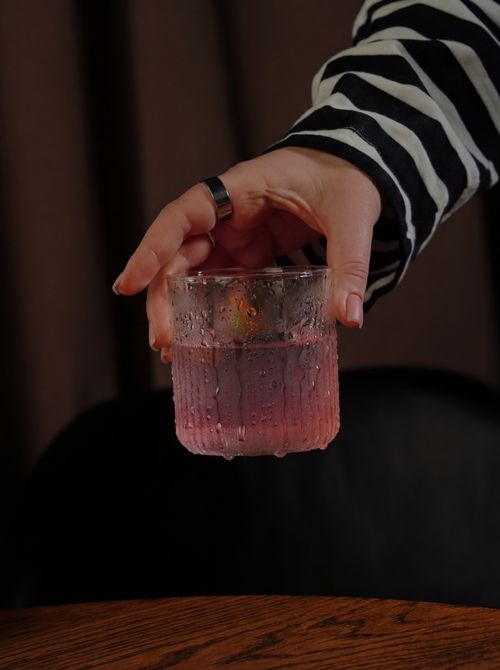 Free Close-up of a hand holding a glass filled with a refreshing pink drink indoors. Stock Photo