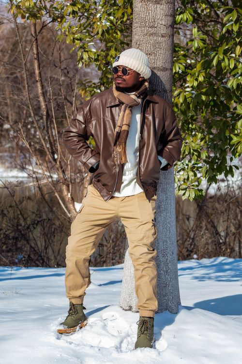 Free Man dressed in winter fashion leaning against tree in snowy landscape. Stock Photo